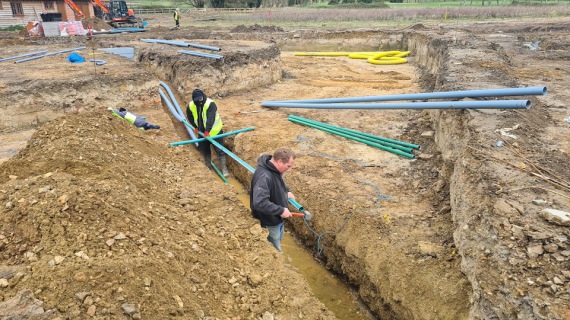 Two men fitting ducting into a trench that will go under a new road.